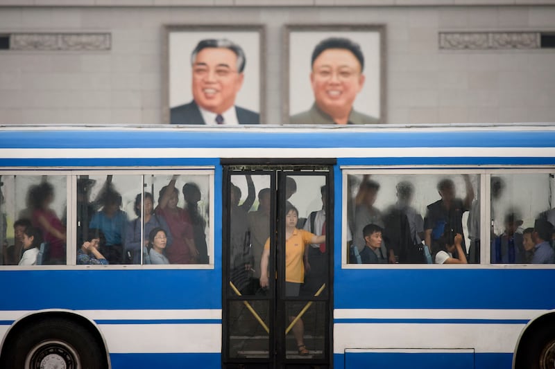 2019년 6월 18일, 평양 김일성 광장에서 통근자들이 버스를 타고 김일성, 김정일 등 북한 전 지도자들의 초상화 앞을 지나가고 있다.