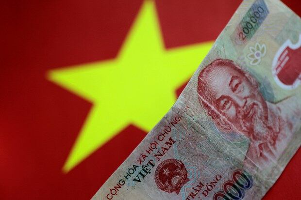 CAPTION: A Vietnamese dong banknote over an image of the Vietnamese flag.