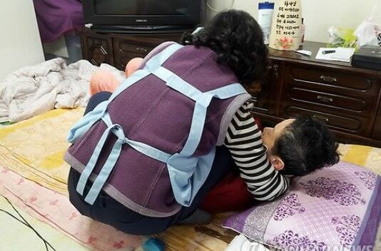 할머니가 요양보호사의 도움을 받으며 힘겹게 몸을 일으키고 있다. 