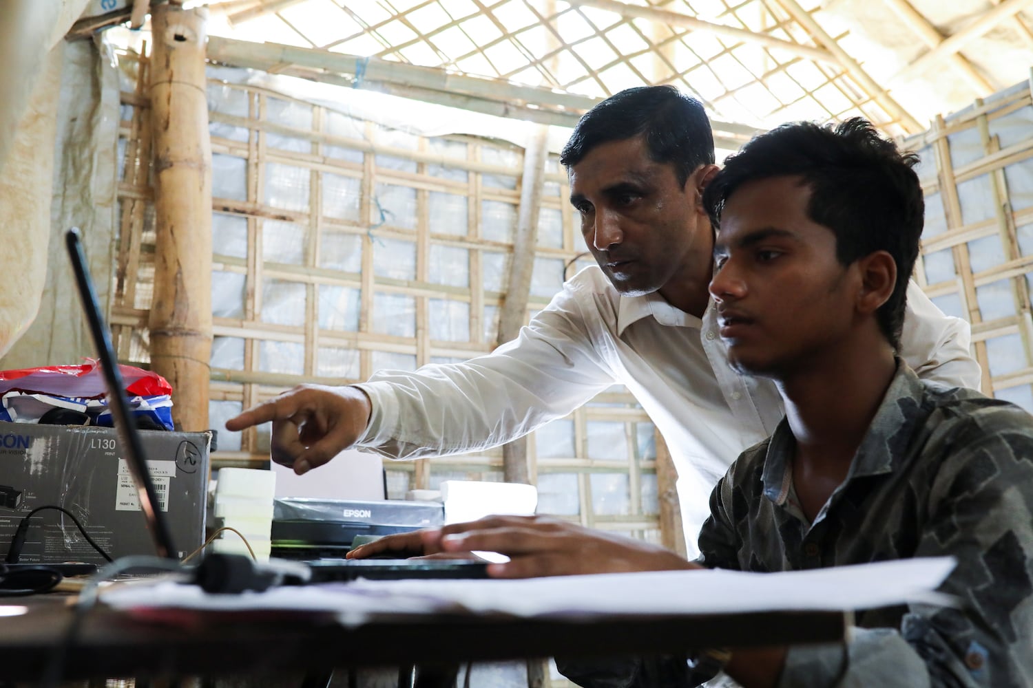 Muhib Ullah, a Rohingya Muslim leader who was killed by suspected militants in the refugee camps in September 2021, helps a computer operator at his office in the Kutupalong camp in Ukhia, Cox’s Bazar, Bangladesh, April 21, 2018.