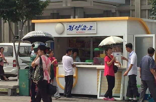 평양역 광장 매점에서 남녀가 아이스크림을 먹으며 활짝 웃고 있다.