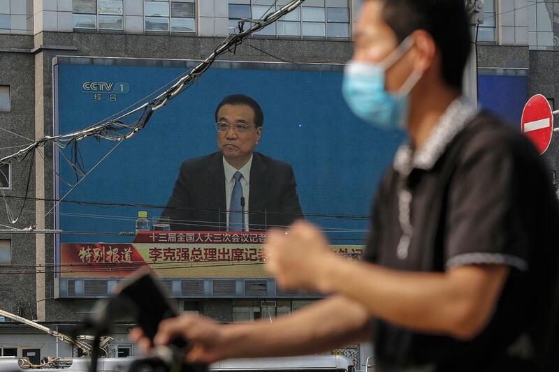 2020年5月28日，一名戴着自行车防护面罩的男子在大屏幕附近经过，屏幕显示中国国务院总理李克强在人大闭幕后的中外记者会上。（美联社）