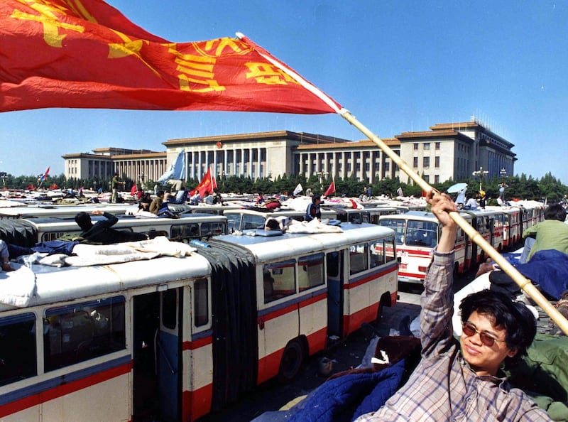 1989年5月23日,学生站在停在天安门广场上的公共汽车顶上挥舞旗帜。(美联社)