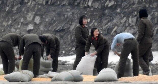 중국 단둥시 외곽에 위치한 수풍댐 인근에서 바라본 북한 평안북도 삭주군에서 북한 여군들이 포대자루에서 곡물로 추정되는 물체를 말리기 위해 바닥에 뿌리고 있다.