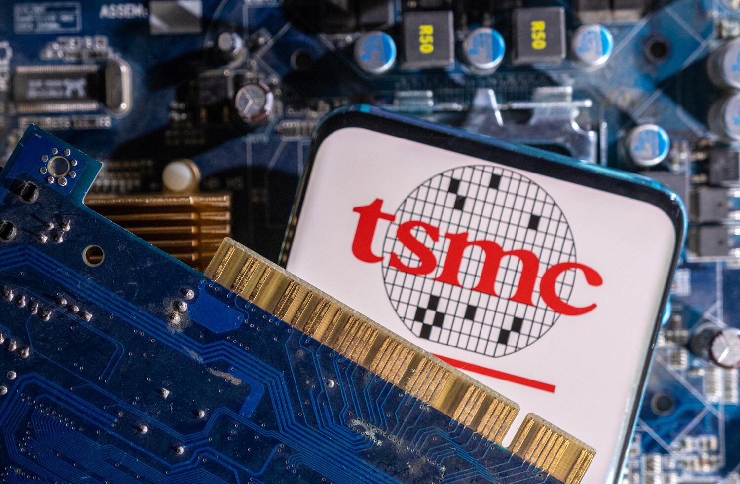The photo illustration displays the smartphone with the Taiwan Semiconductor Manufacturing Company logo and a computer motherboard.
