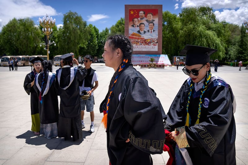 西藏大学理学院的毕业生们站在一张巨幅现任和前任中国领导人的照片前准备合影。(美联社)