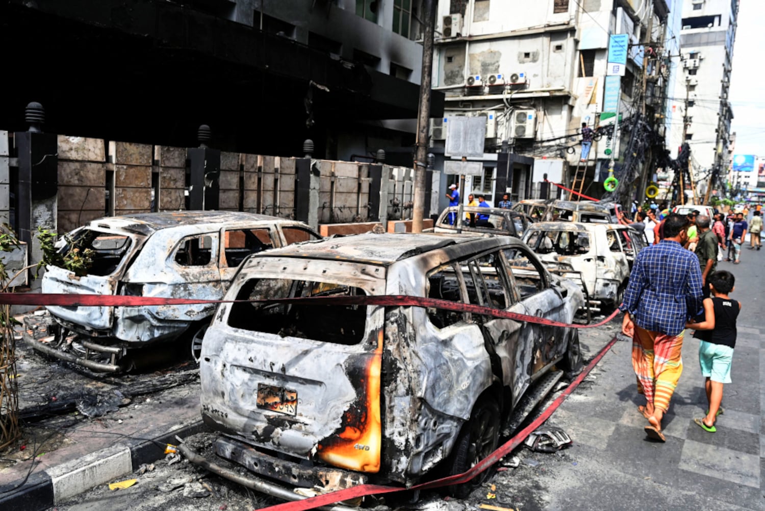 People walk past vehicles burned during unrest in Dhaka, July 19, 2024. (Munir Uz Zaman/AFP)