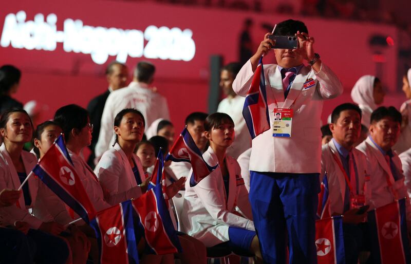 2026년 9월 19일 일본 나고야 팔로마 미즈호 스타디움에서 열린 2026 아이치·나고야 아시안게임 개회식에서 흰색 단복을 입은 북한 선수단 관계자가 스마트폰을 들고 개회식 현장을 촬영하고 있다.