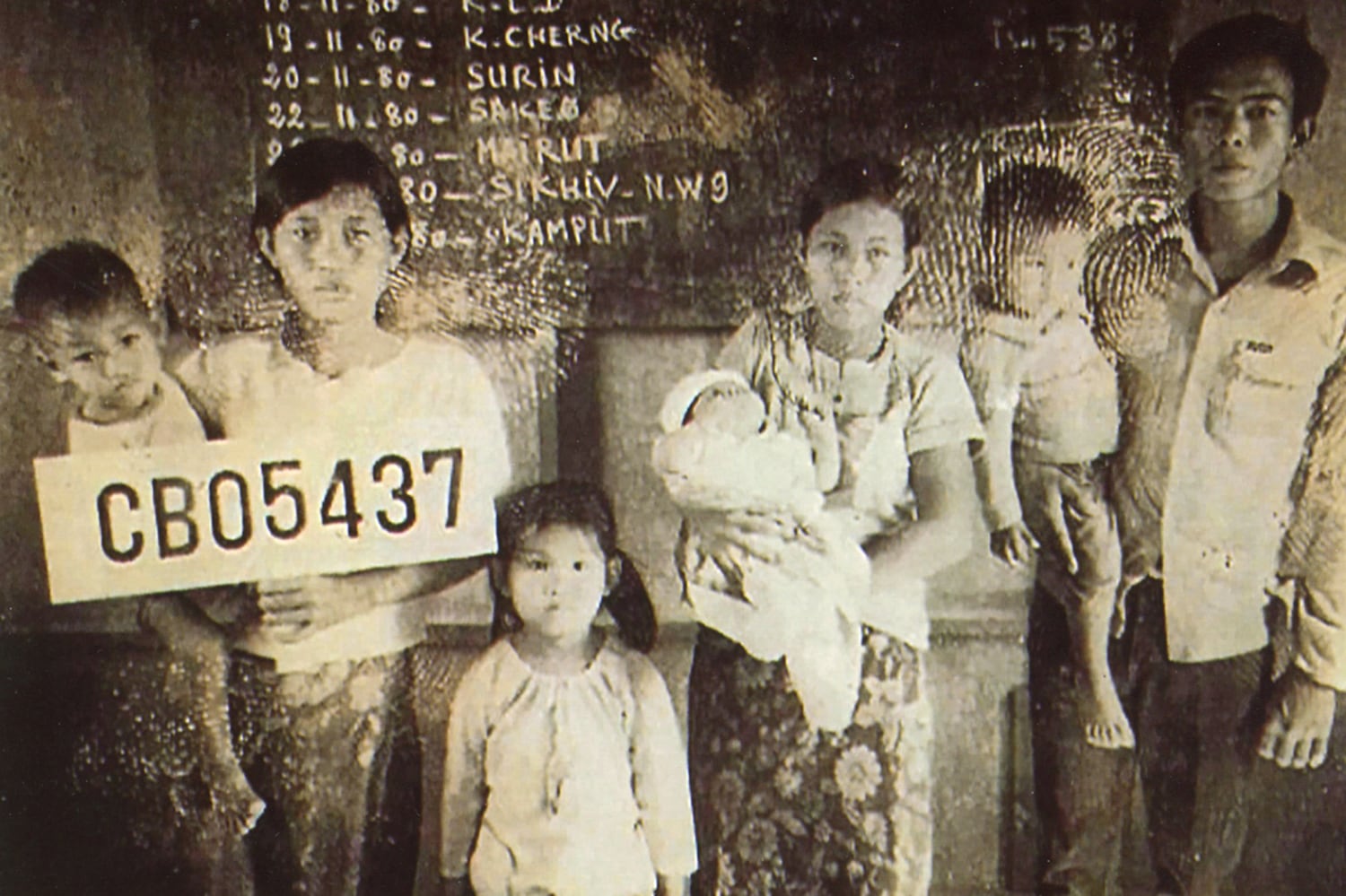 Sarann Nuon, the young girl at center, stands next to her mother, left, who is holding her younger brother and a sign indicating the family’s refugee number.
