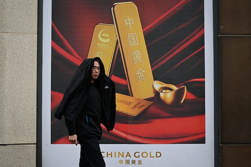 2024年4月10日,北京一名男子在雨天路过一则投资黄金广告。(法新社)