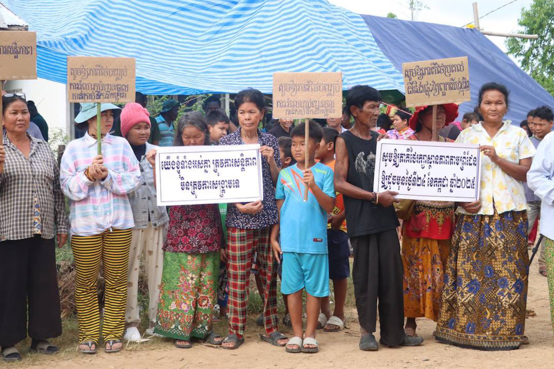 Residents of Prey Chan village hold up banners in protest on August 15, 2025, after Thai soldiers erected barbed wire around their homes and evicted them.
