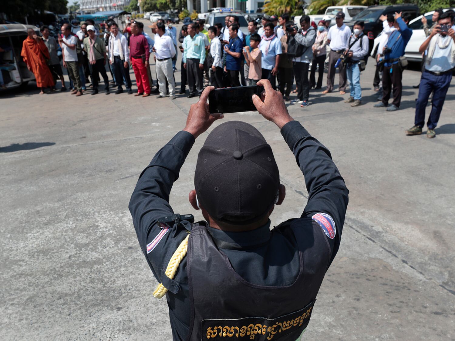 A Cambodia police officer takes photographs of opposition supporters while they wait during a hearing of their former National Rescue Party's President Kem Sokha at an appeals court in Phnom Penh, Jan. 30, 2024.