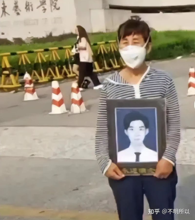 高彦的母亲在高彦生前就读的山东艺术学院校门处举起高彦遗像。(网络截图)