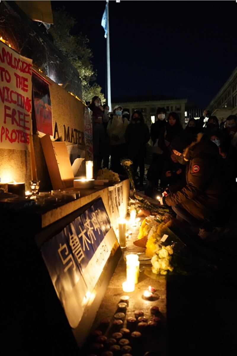 参与集会的学生将“智慧女神”雕像的底座设置成祭台,贴上乌鲁木齐11.24火灾死难者照片和海报,奉上鲜花和蜡烛。(记者艾玛摄)