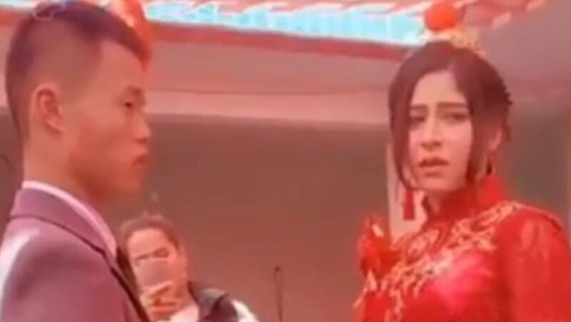 خىتايچە كىيىندۈرۈلگەن ئۇيغۇر قىزنىڭ خىتاي بىلەن ئورۇنلاشتۇرۇلغان توي مۇراسىمىدىكى راھەتسىز ۋە نارازىلىق چىرايى.