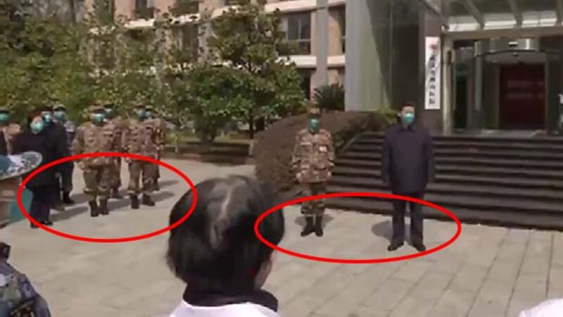 習近平站在報稱是「火神山醫院」的建築物前,但他的影子跟其他人的影子的方向並不一致。(網絡視頻截圖)