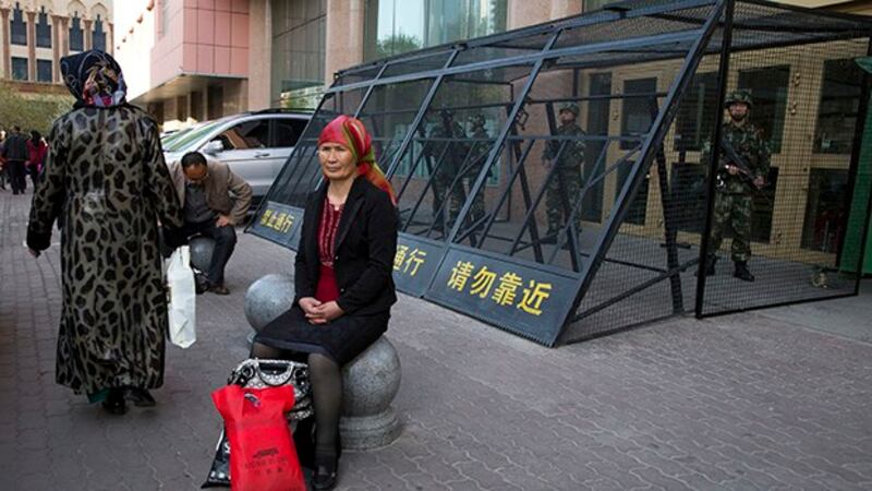 新疆乌鲁木齐街头的维吾尔妇女，背景为持枪的武警。（美联社资料图）