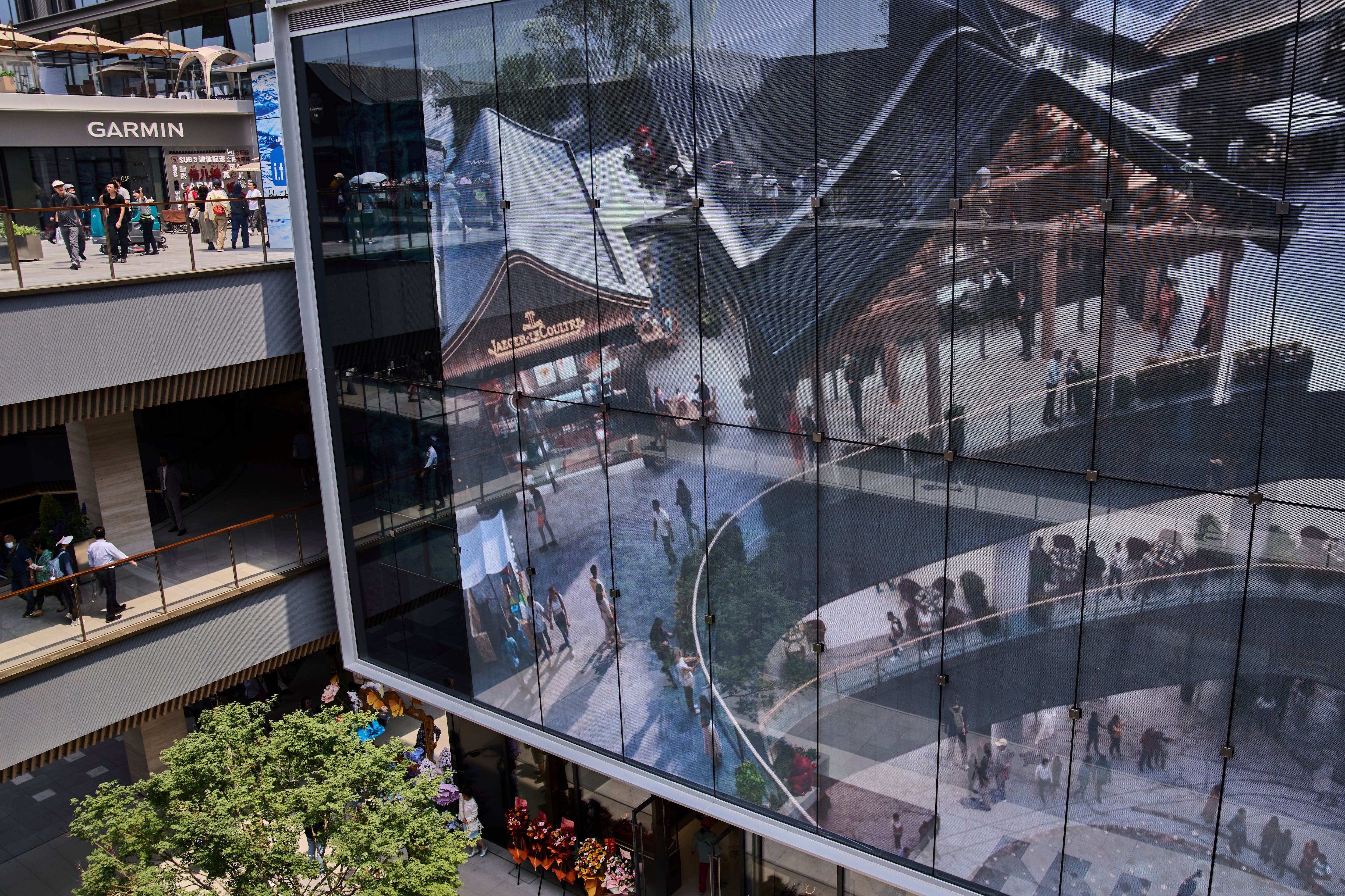 People tour by a projector screen promoting a newly opened outdoor Hutong style shopping mall, in Beijing, Monday, May 26, 2025. (AP Photo/Andy Wong)
