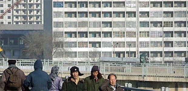 북한 평양거리의 시민들이 매서운바람에 귀를 막고 다리를 건너고 있다. 뒤로보이는 아파트 베란다는 추운날씨를 대비해 비닐로 막아놓은 모습.