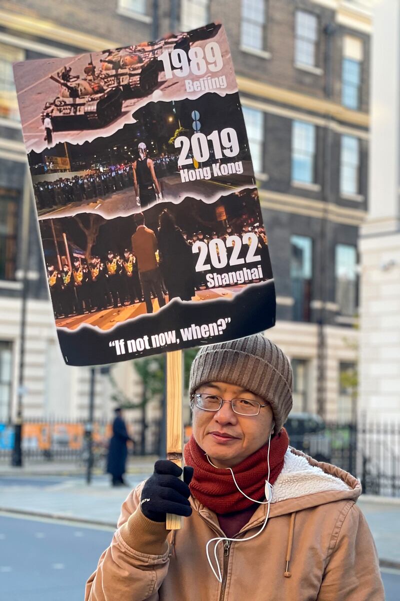 參與抗議的前八九學運領袖邵江舉起海報，描繪八九學運、香港反送中運動，以及「白紙運動」的三代人。（呂熙攝）