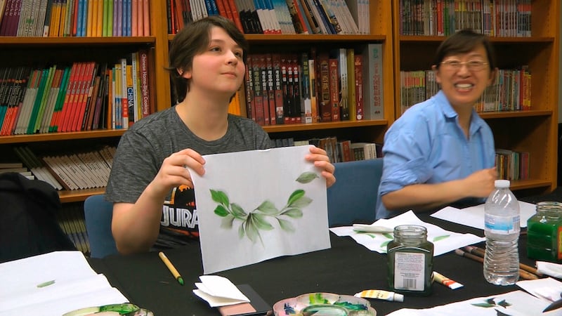 Undergraduate student Moe Lewis, left, shows her watercolor painting of peony leaves at a traditional Chinese painting class at the Confucius Institute at George Mason University in Fairfax, Virginia, May 2, 2018.