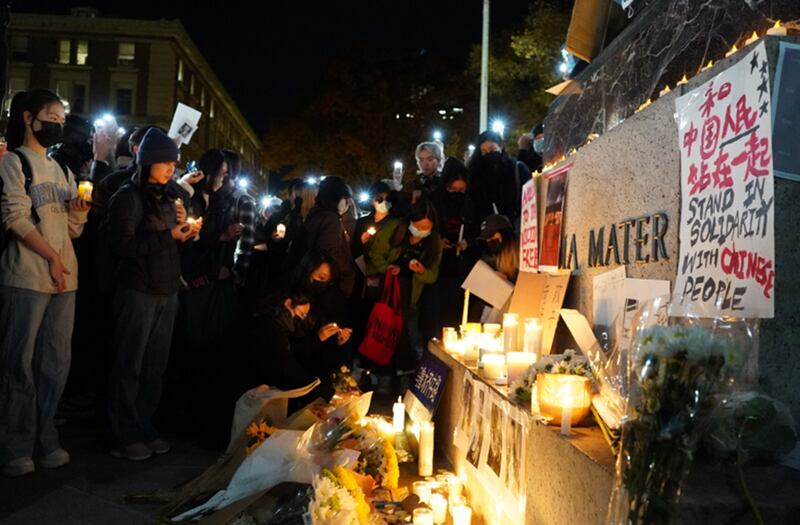 参与集会的学生将“智慧女神”雕像的底座设置成祭台,贴上乌鲁木齐11.24火灾死难者照片和海报,奉上鲜花和蜡烛。(记者艾玛摄)