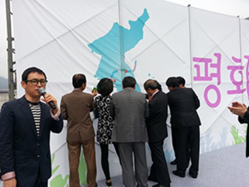 남북경협 기업인들과 시민들이 한반도의 평화와 통일을 염원하는 마음에서 푸른색의 한반도가 그려진 대형 그림판에 평화를 뜻하는 꽃 모양의 종이를 붙이고 있다. RFA PHOTO/ 노재완