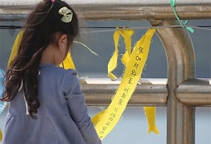 세월호 침몰 사고 발생 24일째인 9일 오전 전남 진도 팽목항을 찾은 한 어린이가 희생자를 추모하고 실종자의 무사귀환을 기원하는 글귀가 적힌 노란색 리본을 만져보고 있다. 