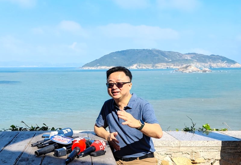 海基会秘书长罗文嘉在大坵岛上受访,后方为福建高登岛。(海基会提供)
