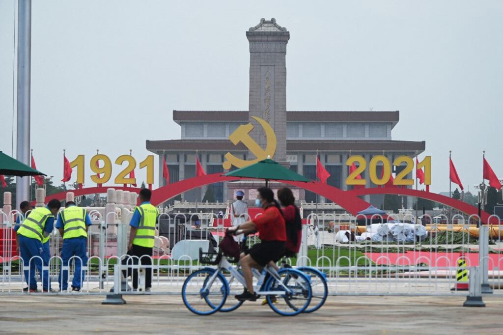 Cyclists ride past as workers adjust a barrier near decorations in Tiananmen Square a day before an event marking the 100th anniversary of the founding of the Communist Party of China, in Beijing, June 30, 2021.