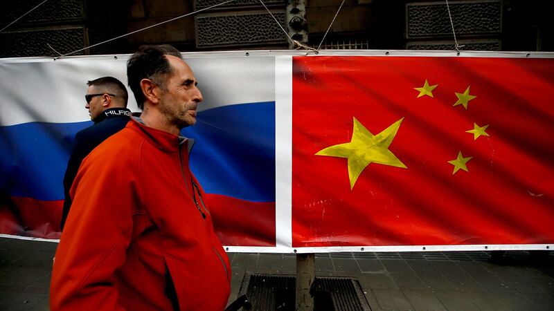 图为，在塞尔维亚首都贝尔格莱德的街道上，人们走过俄罗斯和中国国旗。（美联社）
