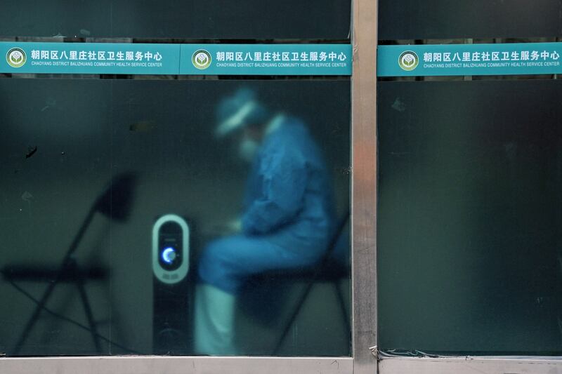 A worker in personal protective equipment keeps warm by a heater near a residential area under lockdown due to COVID-19 restrictions in Beijing, Nov. 29, 2022. Credit: Noel Celis/AFP