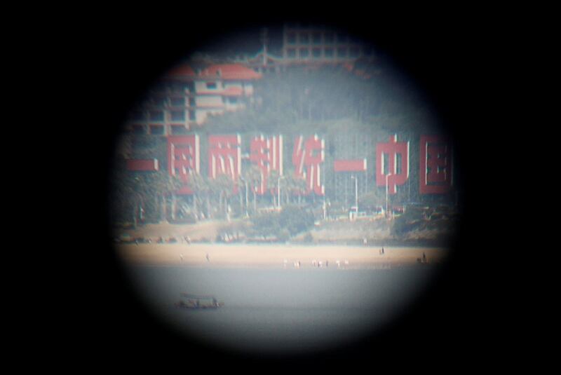 游客在台湾金门烈屿岛的旧军事堡垒上,通过望远镜看到写有“一国两制,统一中国”的横幅。(路透社)