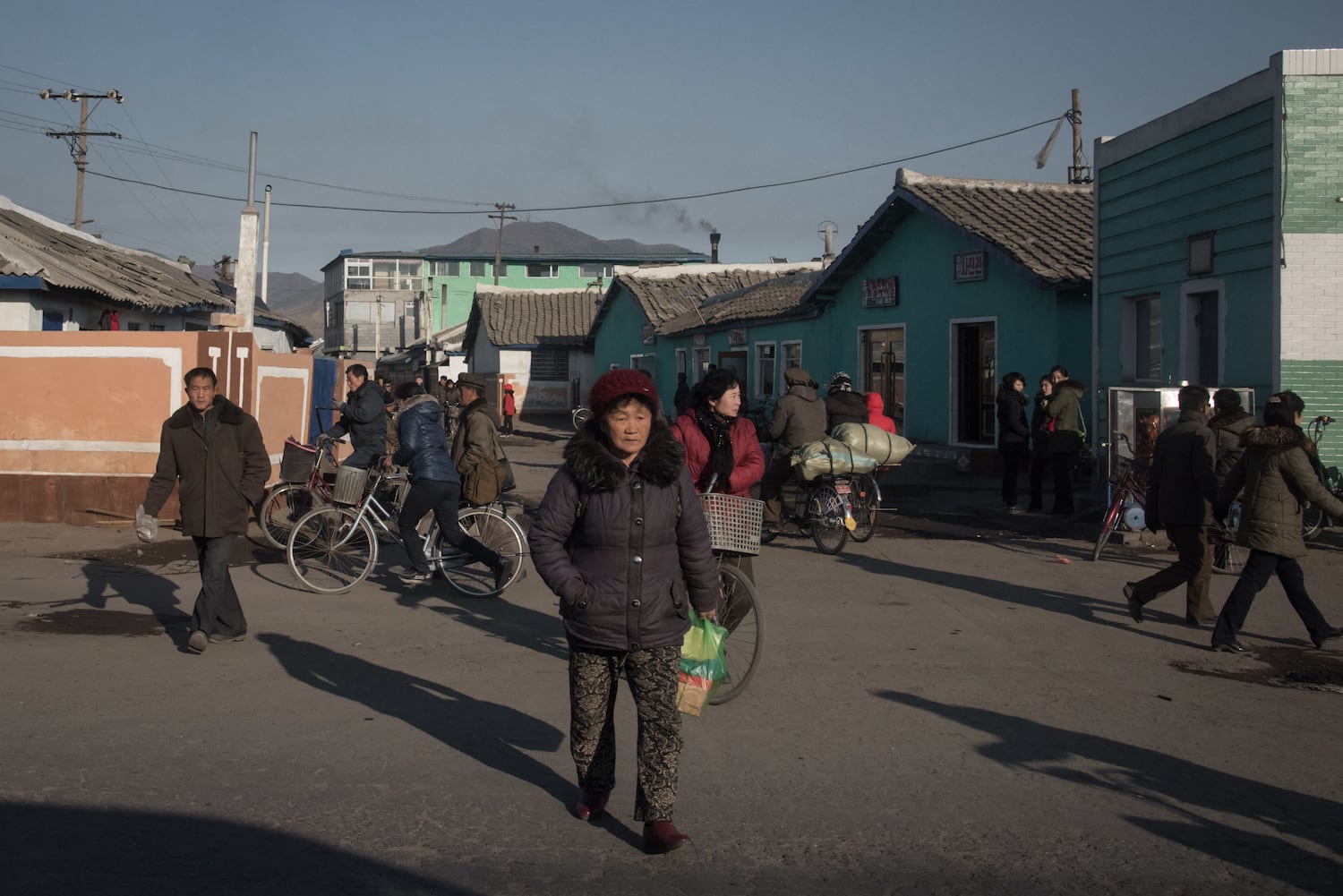 People, wearing coats while walking or riding bicycles,  cross a street on the outskirts of the industrial city of Chongjin on North Korea's northeast coast on November 21, 2017. (AFP Photo/Ed Jones)