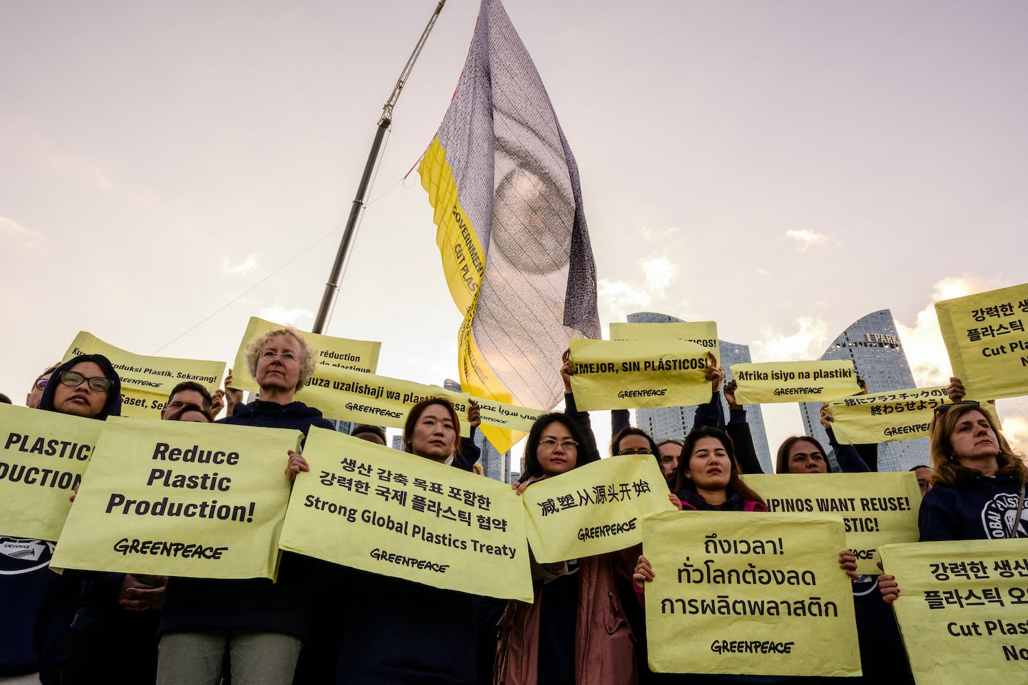 A flag with an eye and the words “Governments, the world is watching, cut plastic production now” is displayed above Greenpeace activists holding placards in Busan, South Korea on Nov. 25, 2024, before the opening of the fifth session of U.N. Intergovernmental Negotiating Committee on Plastic Pollution.