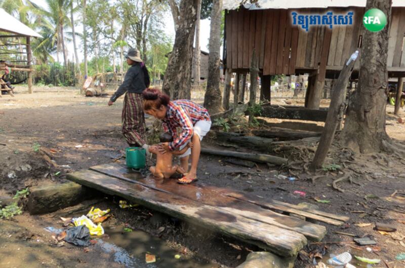 ស្ត្រី​ម្នាក់​កំពុង​យក​ទឹក​អណ្ដូង​ងូត​ទឹក​ឲ្យ​កូន នា​ភូមិ​ចង្គុំទី១ ឃុំ​ទន្លូង ស្រុក​មេមត់ ខេត្ត​ត្បូងឃ្មុំ កាល​ពី​ថ្ងៃ​ទី​២៤ ខែ​មីនា ឆ្នាំ​២០១៥។ 