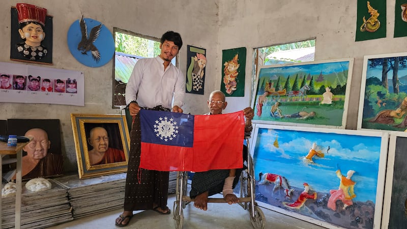ရွှေတံဆိပ်သုံးဆုရ ပန်းချီ၊ ပန်းပု ဗိသုကာပညာရှင် ဦးမြသောင်းကို သူ ဖန်တီးခဲ့သော နိုင်ငံတော်အလံနှင့်အတူ ၂၀၂၄ ခုနှစ် နိုဝင်ဘာ ၂၀ ရက်နေ့က တွေ့ရစဉ်။ (Photo: RFA)