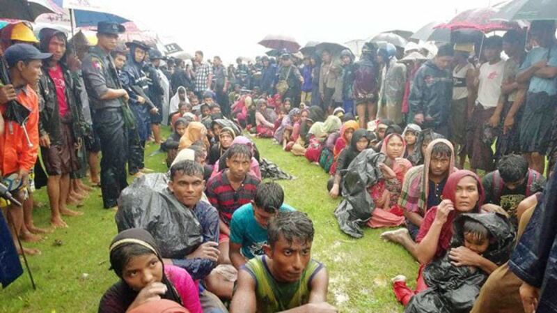 Rohingya refugees from Bangladesh sit in the rain after they and their wrecked boat washed up on a beach in Rathedaung township, western Myanmar's Rakhine state, June 12, 2018.