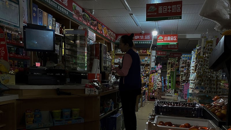2021 年 9 月 29 日，辽宁省沈阳市停电期间，一名妇女使用汽油发电机供电的灯泡从小型市场购买杂货。（美联社）