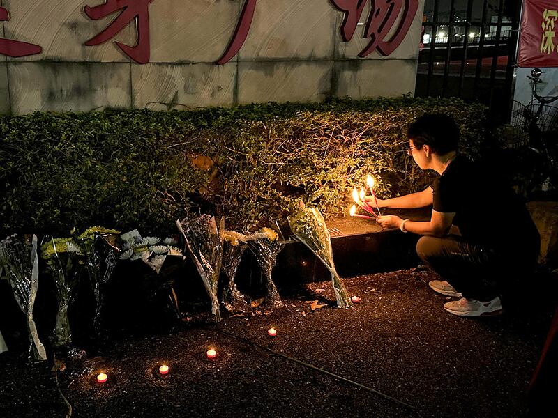 A woman lights candles near floral tributes outside a sports center, Nov. 12, 2024, in Zhuhai, China, where a car ran into a crowd of people.