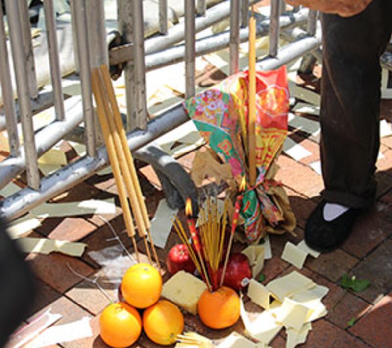 2015年6月6日，在中聯辦外，示威者為李旺陽舉行路祭，在地上擺放食物和香燭，又向鐵欄內撒溪錢（冥錢）。（粵語組殷可靜攝）