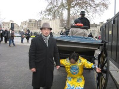 图片：台湾当代艺术家黄瑞芳在伦敦塔展示《人身保护令》行动艺术，以书生囚犯雕塑铐上“河蟹“和谐“枷锁坐在英国传统马车。马车随后在伦敦主要道路行走，最终走到中国驻英使馆。（张安安摄）