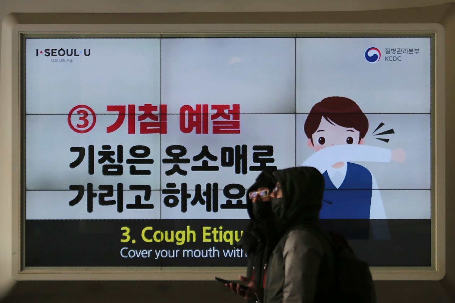 마스크를 쓴 시민들이 기침 예절을 알리는 전광판 앞을 지나가고 있다.