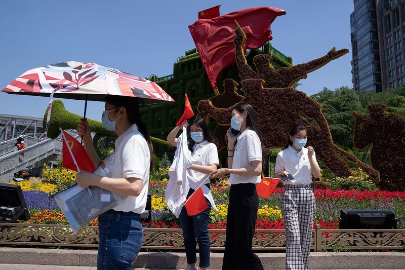 资料图片：2021 年 6 月 22 日，在北京即将举行中共建党百年大会，市民手持共产党旗帜走过花卉装饰。 （美联社）