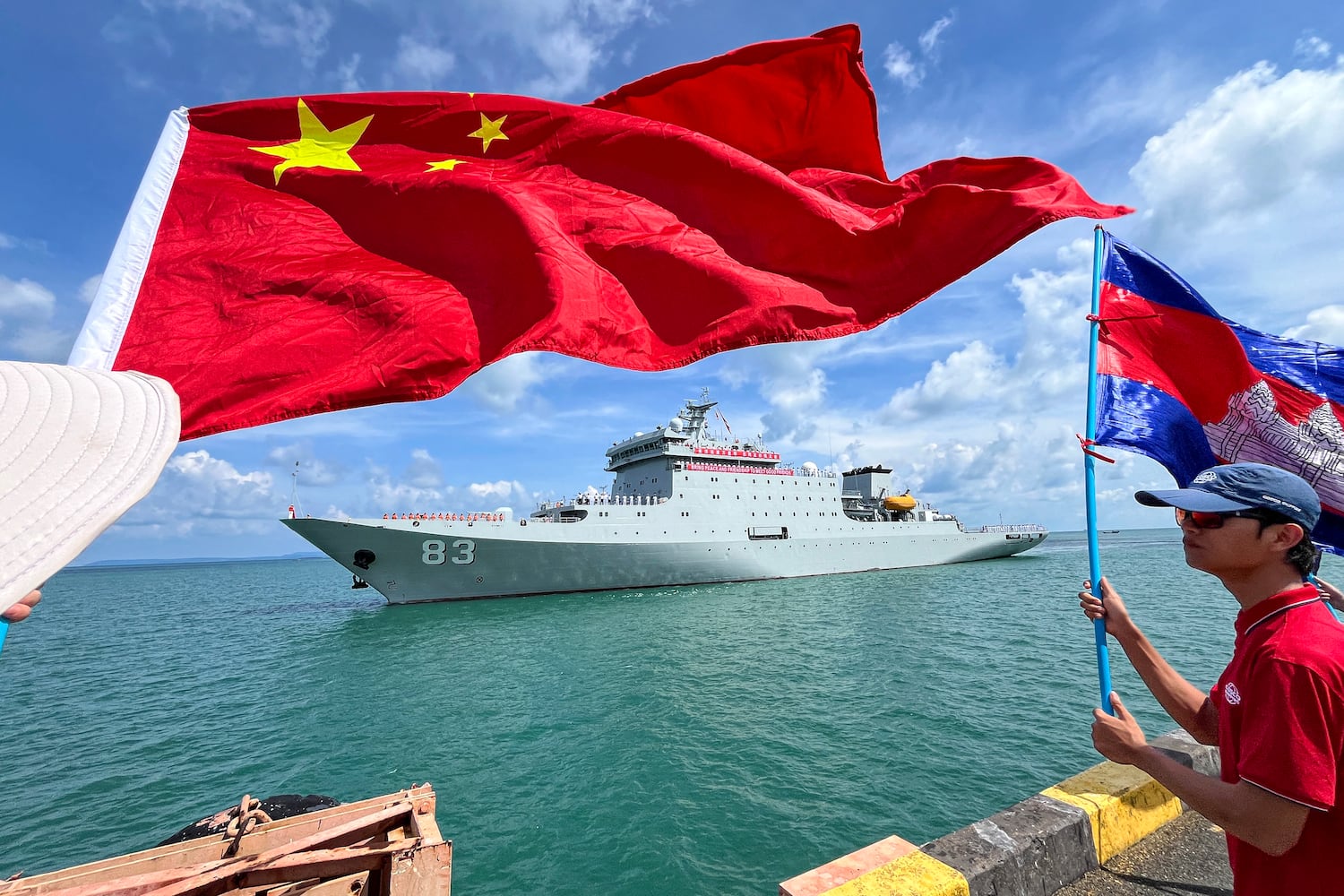 People wave Cambodian and Chinese flags as the Chinese ship Qi Jiguang prepares to dock with a banner reading 