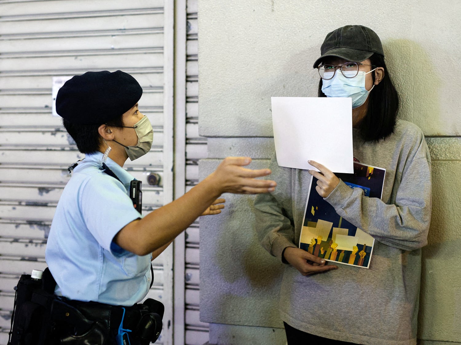 A police officer asks a woman to leave as she holds white sheets of paper during a commemoration of the victims of a fire in Urumqi, in Hong Kong Kong, China November 28, 2022.  (REUTERS/Tyrone Siu)