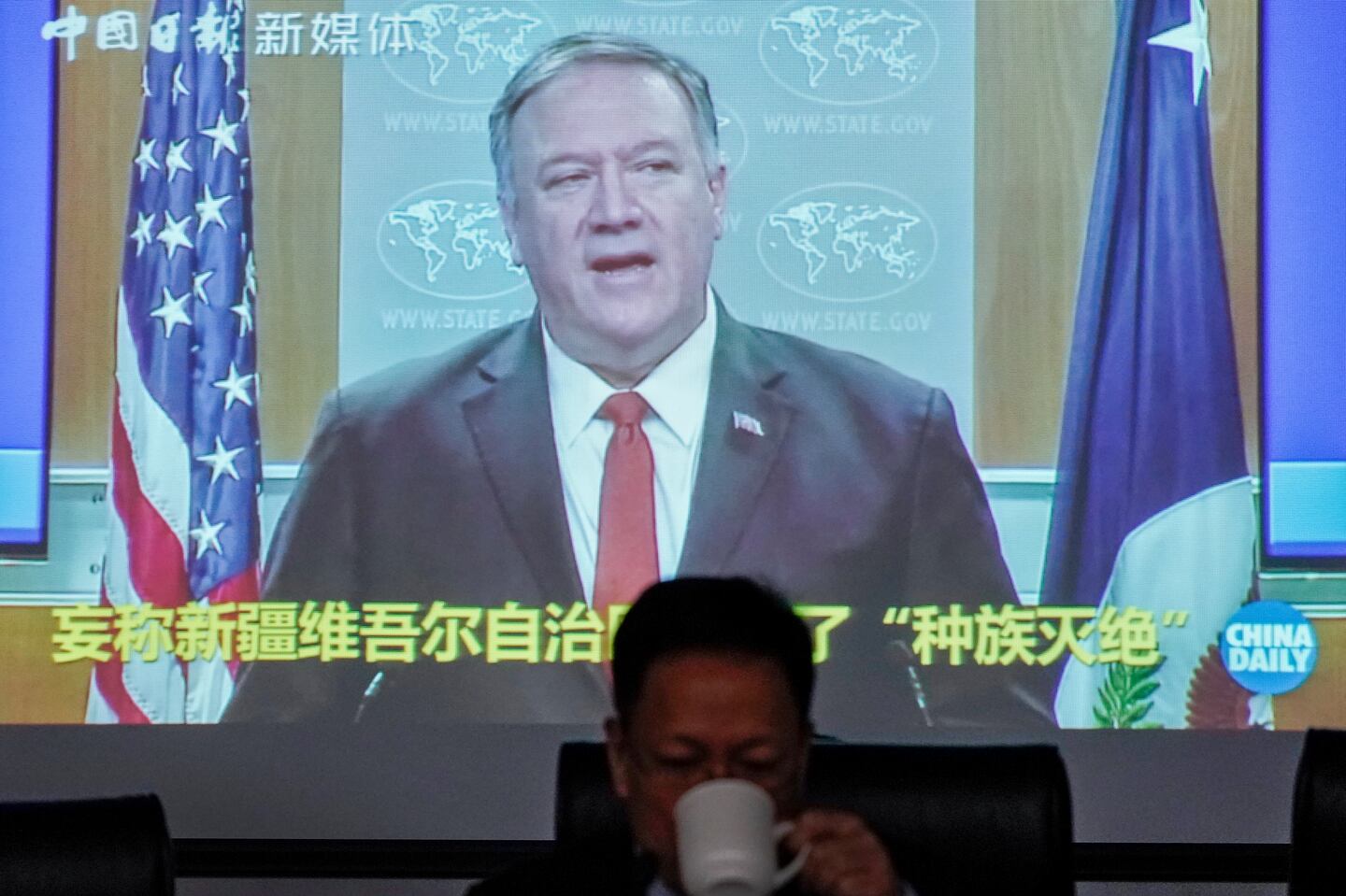 Xu Guixiang, a spokesperson for Xinjiang's Communist Party, drinks as a screen showing a footage of former U.S. Secretary of State Mike Pompeo, at the Ministry of Foreign Affairs office in Beijing, Monday, Feb. 1, 2021. Xu accused  Pompeo of trying to undermine Beijing's relations with President Joe
