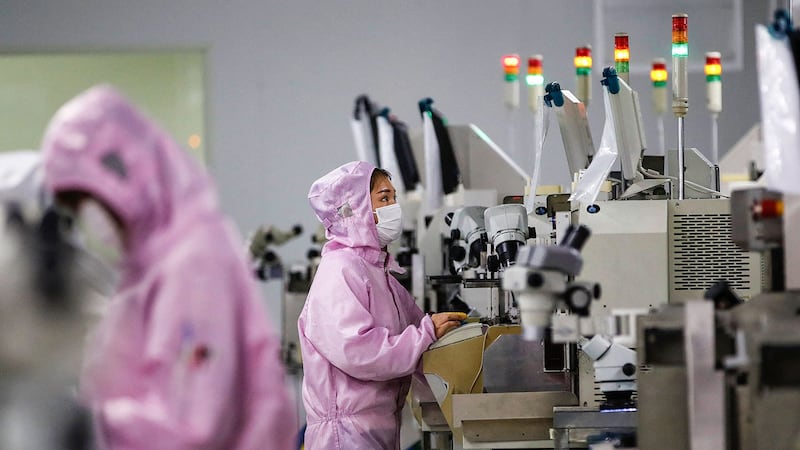 2020 年 2 月 16 日，员工戴着口罩和防护服在江苏省泗洪市的一条智能芯片生产线上工作。（法新社）
