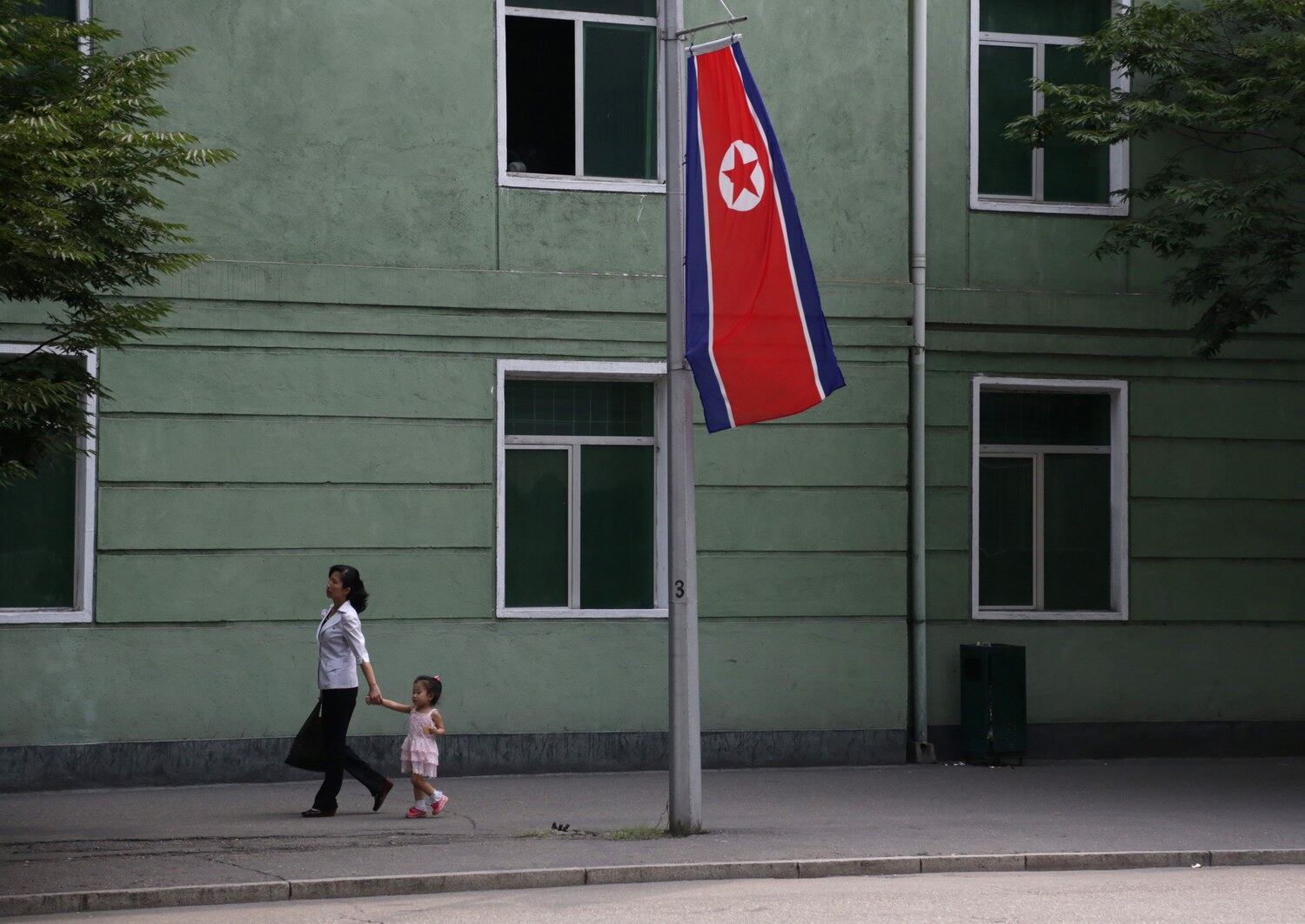 2015년 8월 16일, 북한 평양에서 광복절 기념 행사의 일환으로 게양된 북한 국기 앞을 한 여성과 딸이 지나가고 있습니다.